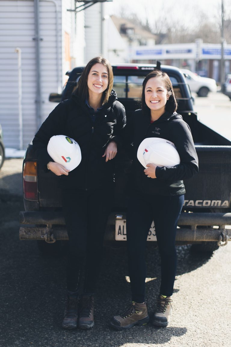 The Bridgit founders standing in front of a truck with hard hats in their hands.