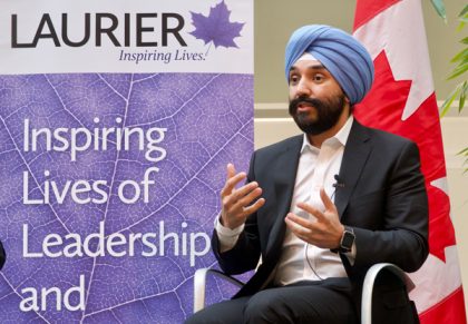 Minister Navdeep Bains speaks at Wilfrid Laurier University beside a WLU banner